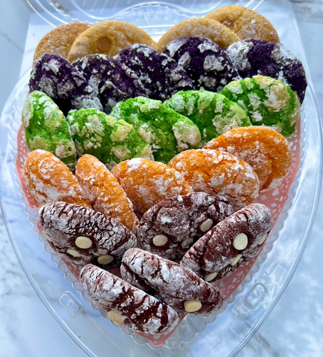Assorted colorful cookies in a heart-shaped container on a marble surface.